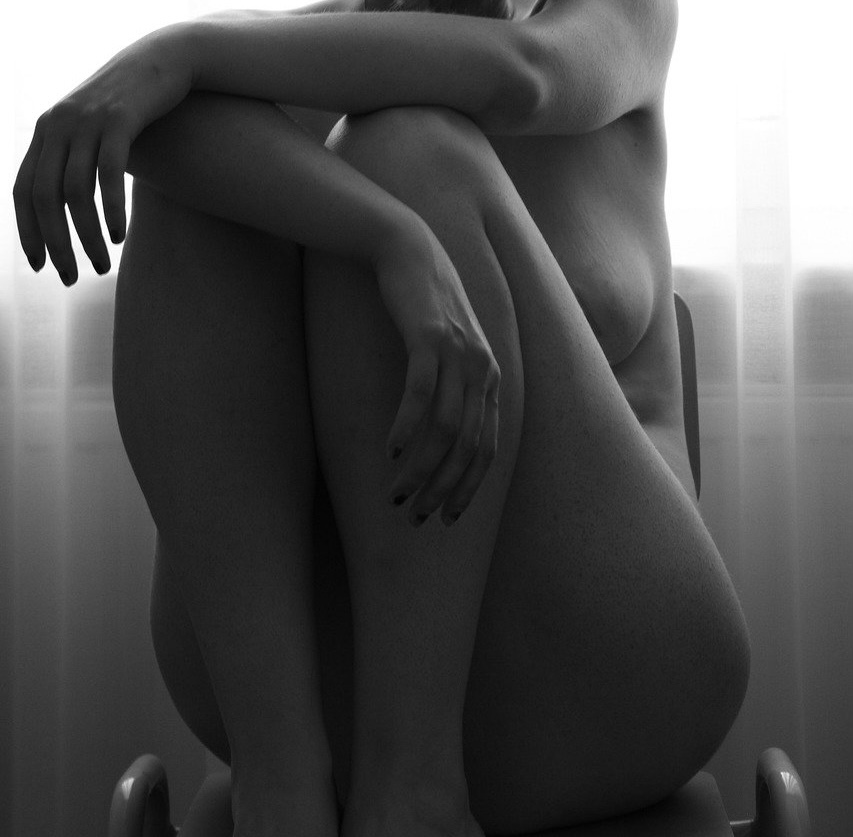 A nude woman sits on a chair in front of a window of a spa for Tantra erotic massage in Istanbul, the light casting delicate shadows around her.